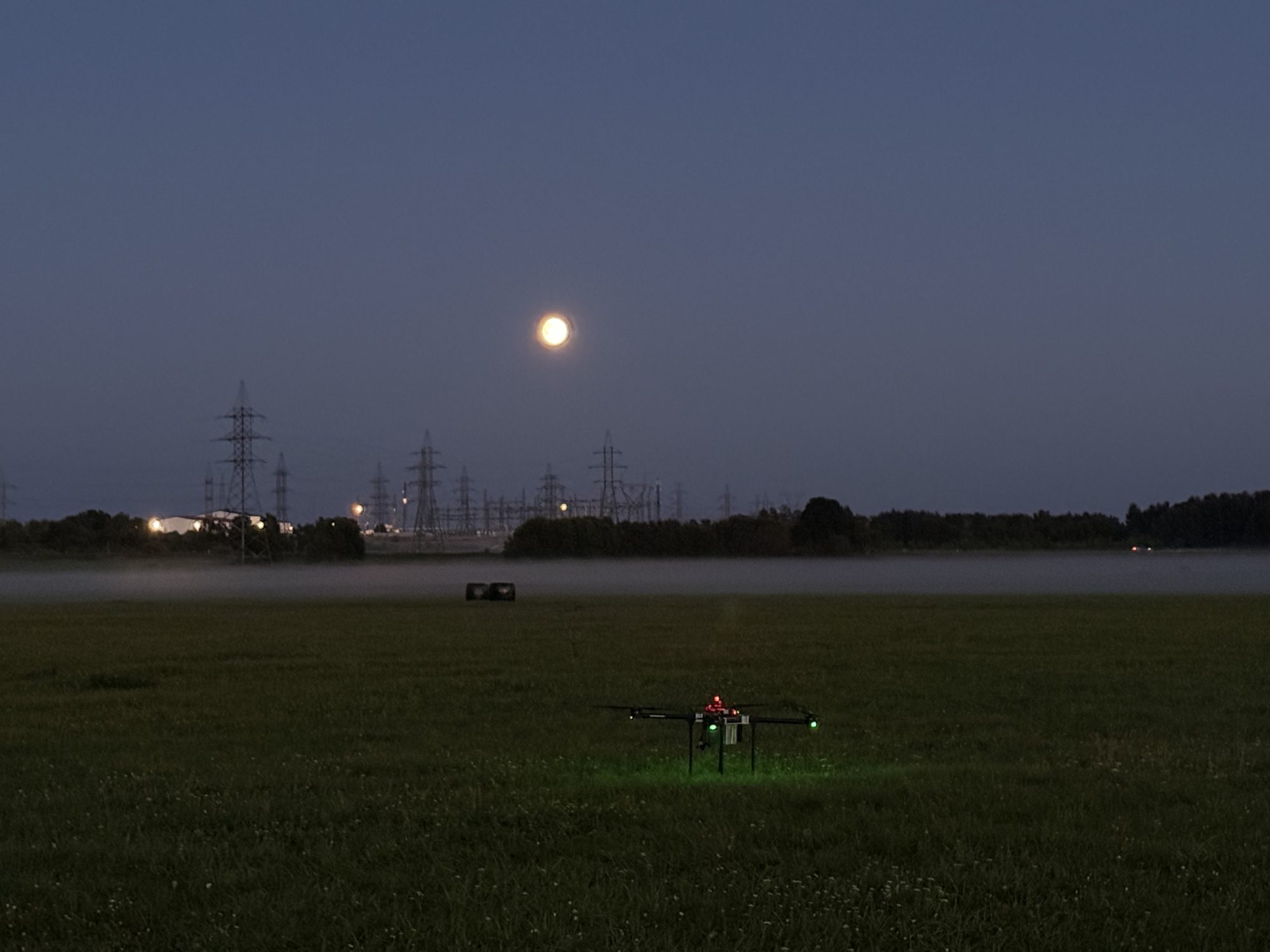 Our drone on a grass field at dusk with its navigation lights on.